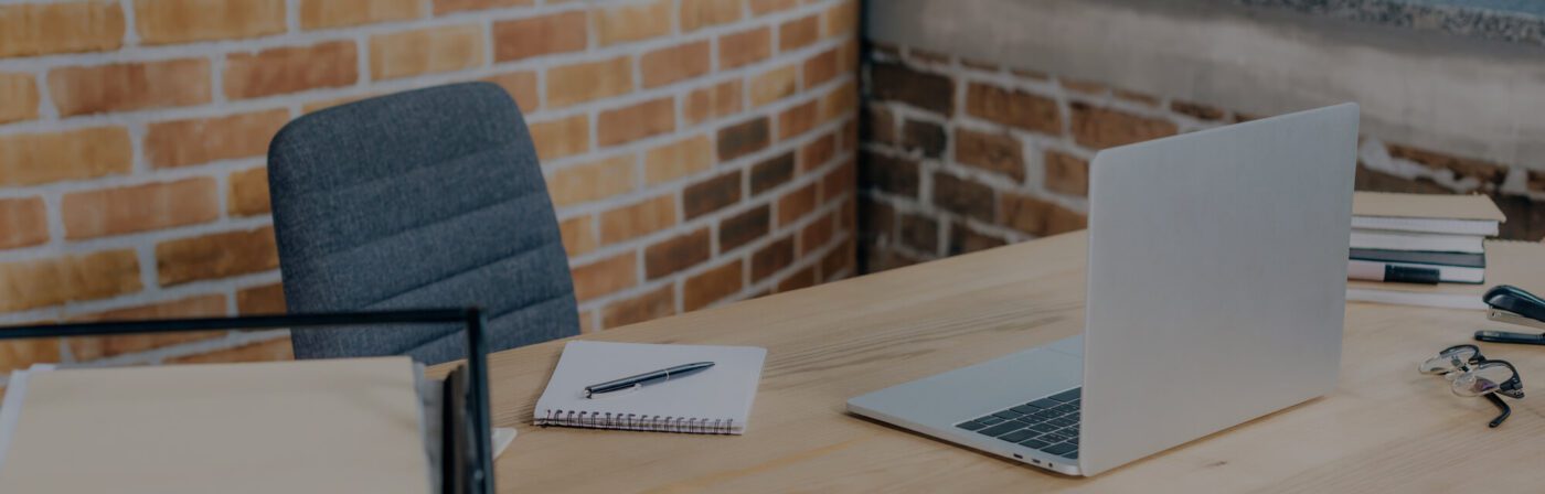 Empty desk with open laptop against brick wall